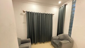 A room with two grey armchairs, a dark curtain, and a tiled floor. - Luciya The Boutique Hotel (Bengaluru)
