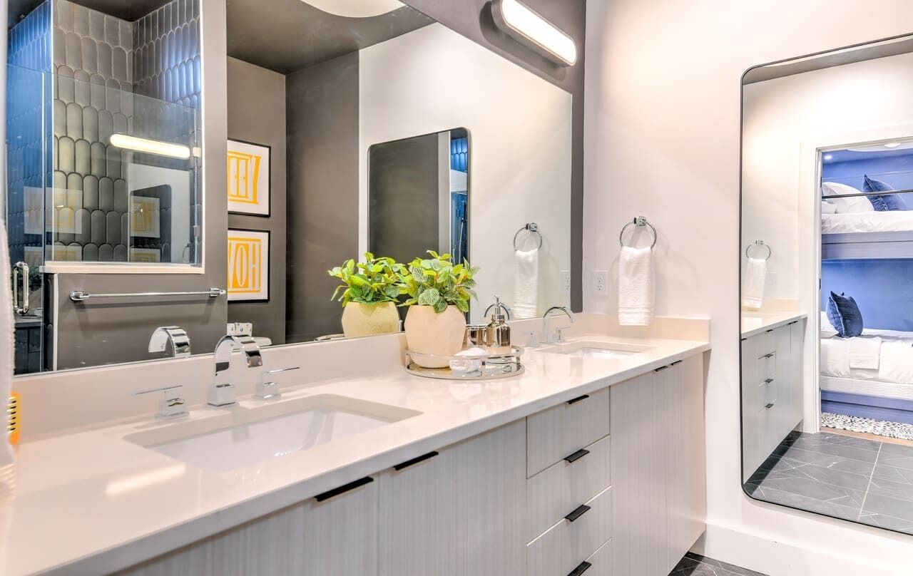 Un baño moderno con un espejo grande, dos lavamanos, una planta en maceta y zona de ducha.