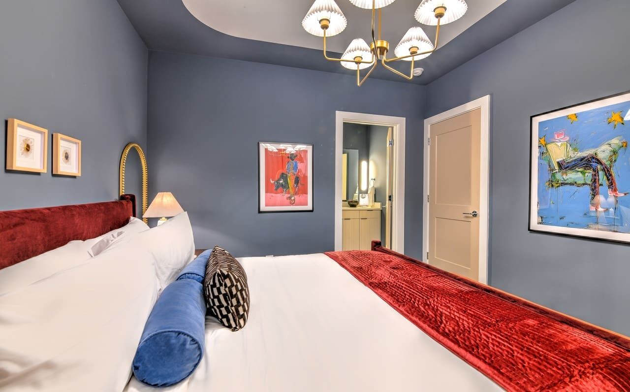 Une chambre à coucher avec un grand lit, un plaid rouge, un lustre et des œuvres d’art accrochées aux murs.