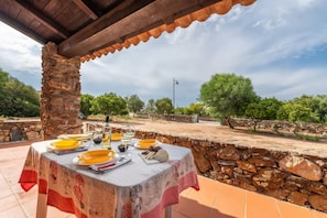 An outdoor dining area with a table set for two, surrounded by stone walls and greenery. - Beachside Apartment for a Relaxing Holiday (Olbia)