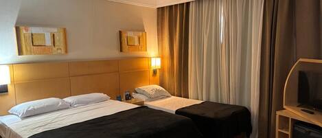 A hotel room with two beds, a TV, and a desk.