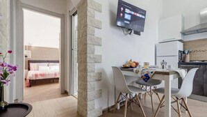 A modern hotel room with a stone accent wall, a dining area with a table and chairs, a bed with a wooden headboard, and a TV mounted on the wall. - Cozy Flat Steps From Porto Torres Beaches (Porto Torres)