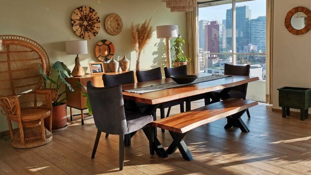 A modern dining area with a wooden table, black chairs, and a woven chair. There are decorative plates on the wall, a hanging light fixture, and a view of the city through large windows. - Bright & Spacious Apartment with Mexico City Views – Polanco (Ciudad de México)