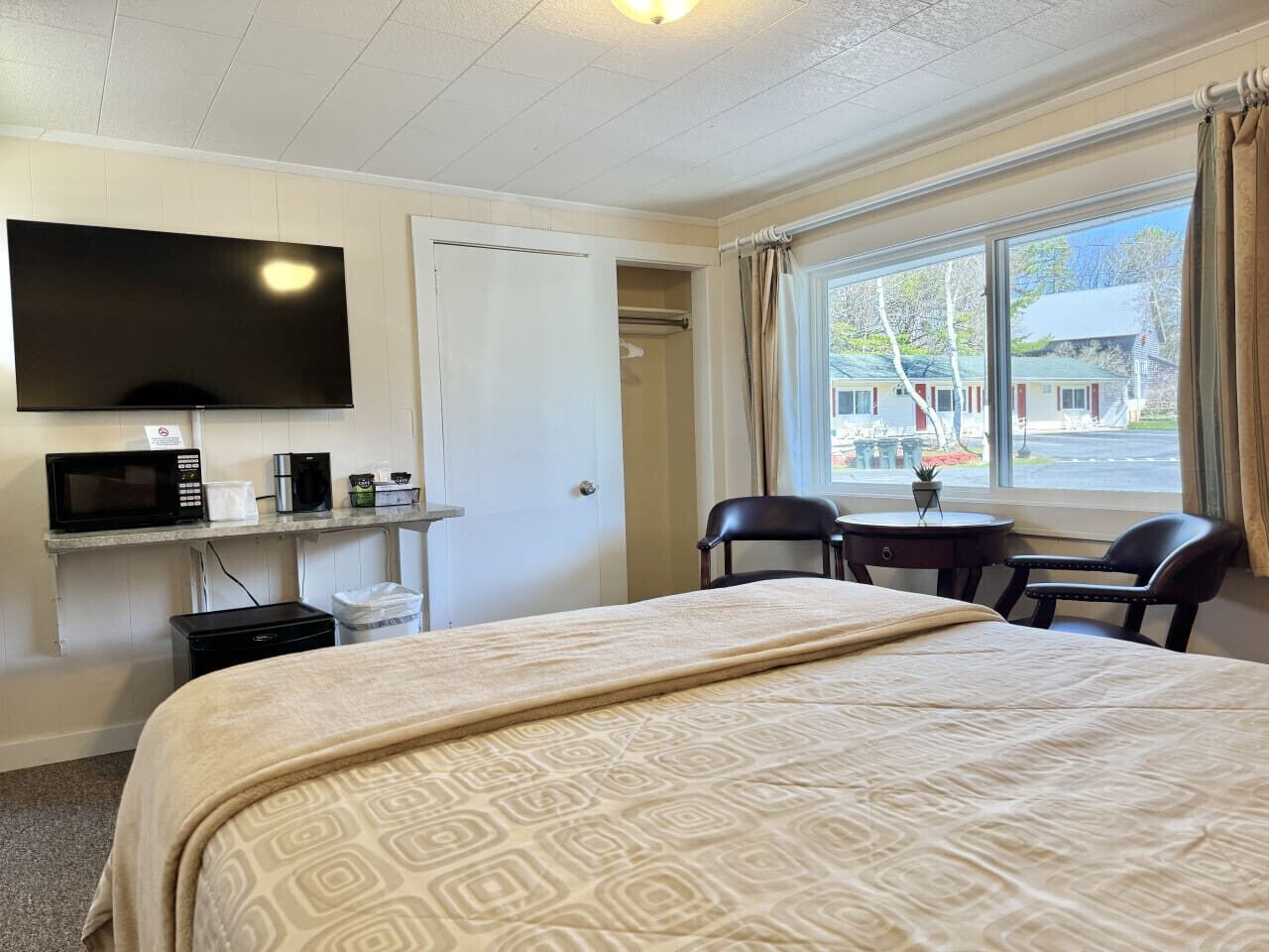 Een hotelkamer met een bed, een televisie, een magnetron, een klein tafeltje met stoelen en een raam met gordijnen.