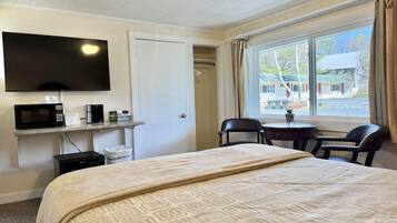 Een hotelkamer met een bed, een televisie, een magnetron, een klein tafeltje met stoelen en een raam met gordijnen.