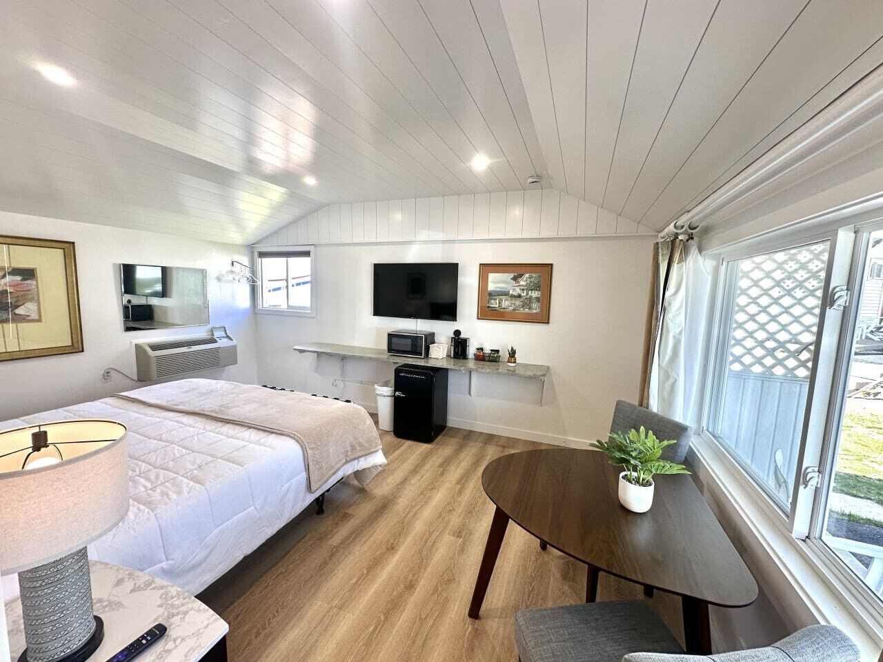 A compact room with a bed, a desk, a chair, a TV, and a window with a view.