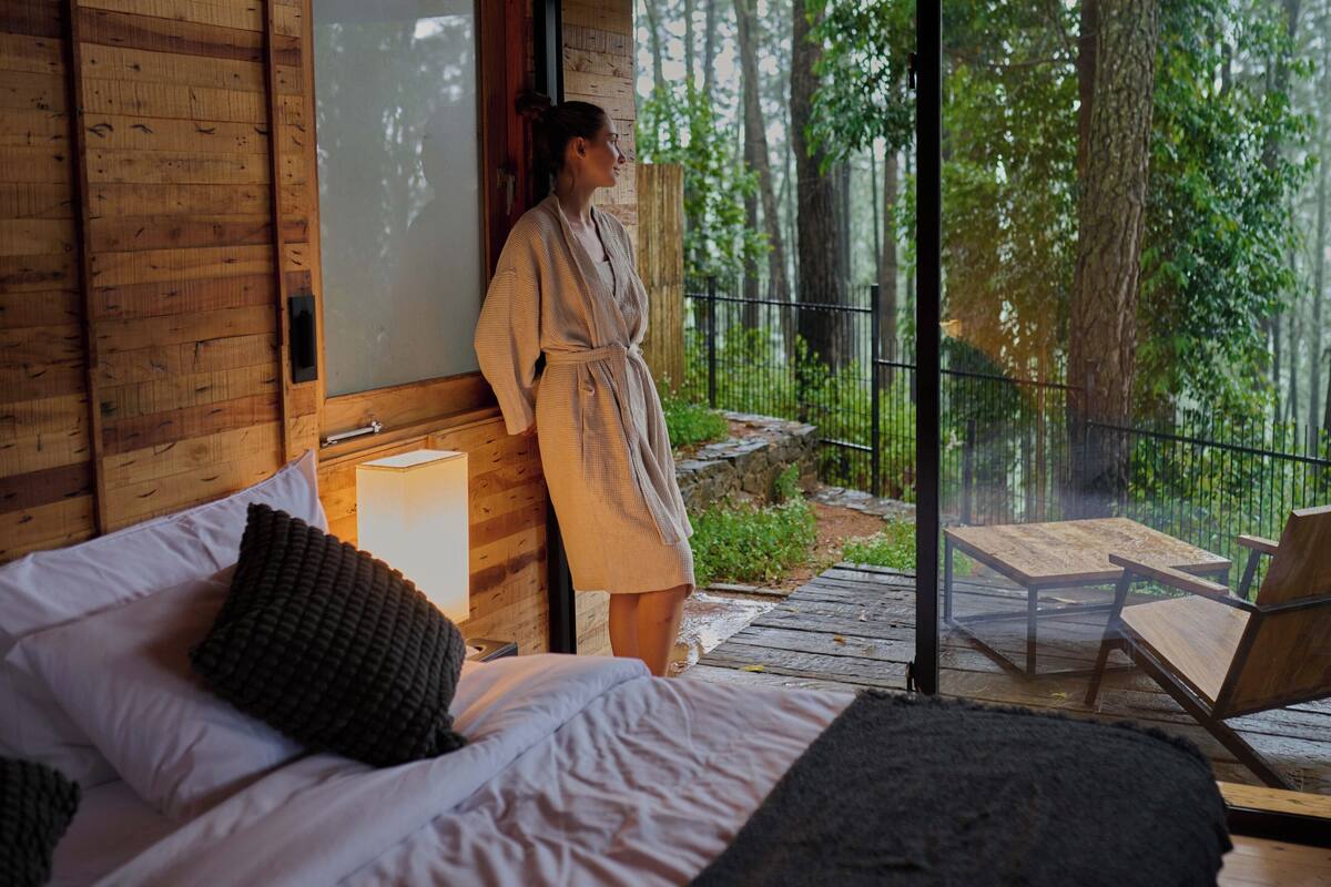 Een houten hut met een bed, een houten tafel en een balkon met uitzicht op een bos.
