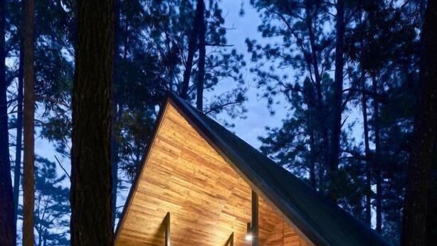 A modern wooden cabin with a sloped roof, built into a forested area. It features a large deck with outdoor seating and a stone pathway leading to the entrance. - Kaya Retreat (Diyatalawa)