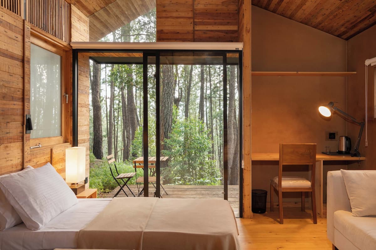A wooden cabin with a large sliding glass door, a bed, a desk, and a chair.