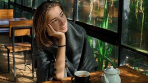 A person sitting at a wooden table with a teapot and cup, near large windows with hanging planters. - Kaya Retreat (Diyatalawa)