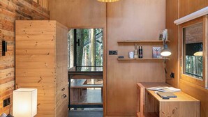 A wooden room with a bed, bedside lamp, desk, shelves, and a hanging light fixture. - Kaya Retreat (Diyatalawa)