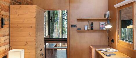 A wooden room with a bed, bedside lamp, desk, shelves, and a hanging light fixture.