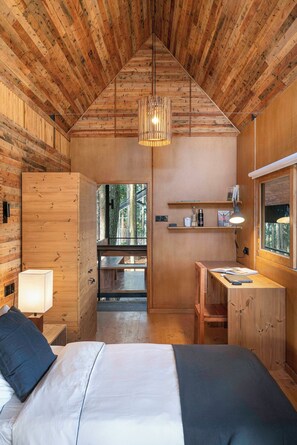 Une pièce en bois comprenant un lit, une lampe de chevet, un bureau, des étagères et un luminaire suspendu.