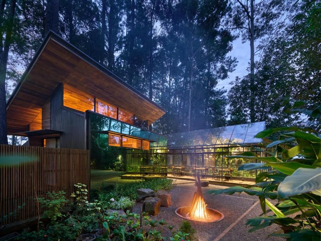 Ein modernes Gebäude mit Holzfassade, einem Wintergarten aus Glas und einem Feuerkorb im Garten.