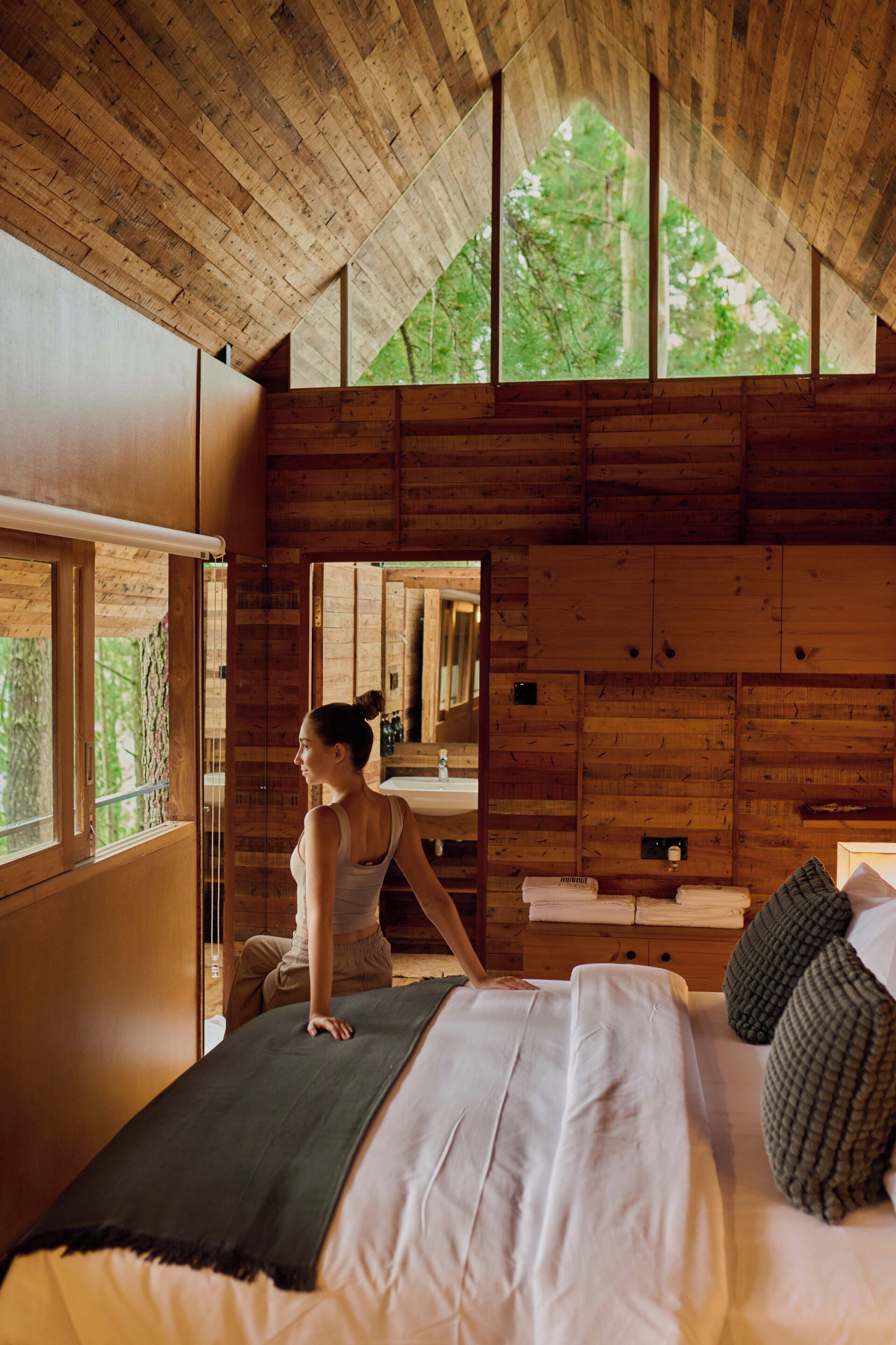Een houten chalet van binnen, met een bed, een raam en een spiegel.