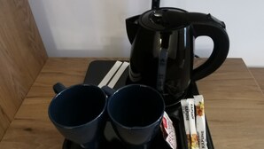 A tray with two black cups, a black electric kettle, and two packets of Kafune instant coffee on a wooden table. - Pensiunea Rasnov (Rasnov)