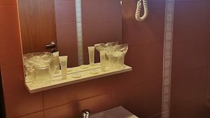 A bathroom with a white sink, a mirror, a hairdryer, and toiletries on a shelf. - Pensiunea Rasnov (Rasnov)