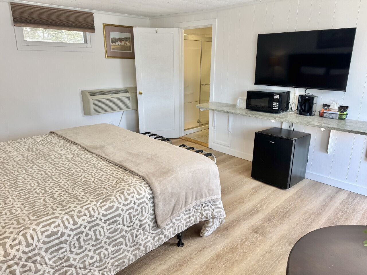 Un dormitorio con cama, televisión, microondas, cafetera y refrigerador pequeño.