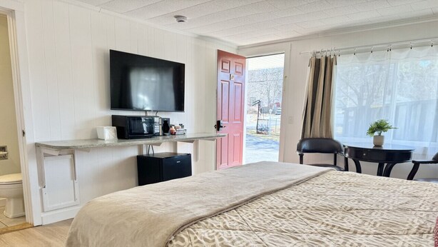 A hotel room with a bed, a TV, a coffee machine, a desk, and a window with curtains. - Gallagher`s Travels Room 2 (King Bed) (Bar Harbor)