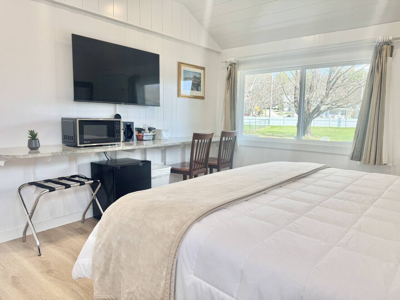 Habitación de hotel con una cama grande, un televisor montado en la pared, un escritorio con microondas y una ventana con cortinas.