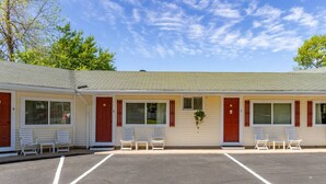 Un motel composé de deux unités, chacune dotée d’une porte rouge, de volets blancs et d’un petit espace porche avec des chaises blanches.
