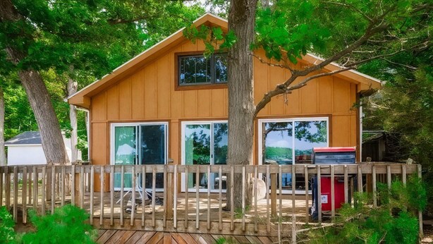 A wooden cabin with large windows, a deck, and a fenced area. - Charming Stone Cottage On Lake James / Lone Tree Point (Angola)