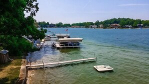 A dock with boats, a small boat on the water, and a dock extending into the lake. - Charming Stone Cottage On Lake James / Lone Tree Point (Angola)