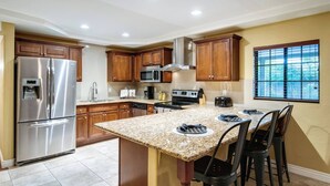 Eine moderne Küche mit Granitarbeitsplatten, Edelstahlgeräten, Holzausbau und einer großen Kücheninsel mit Barhocker.