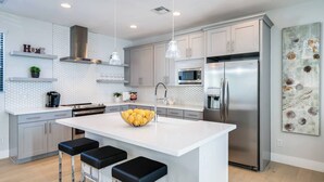 Una cucina moderna con una grande isola, elettrodomestici in acciaio inossidabile, illuminazione a sospensione e un design minimalista.