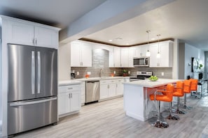 A modern kitchen with stainless steel appliances, white cabinetry, and a central island with bar stools. - Stylish Scottsdale Home & Pool Table (Phoenix)