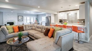 A modern living room with a sectional sofa, a glass coffee table, and a kitchen area with a bar. - Stylish Scottsdale Home & Pool Table (Phoenix)