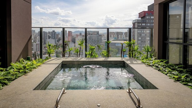 Una piscina en la azotea con vistas a la ciudad, rodeada de plantas y arquitectura moderna.