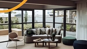 A modern living room with a sofa, coffee table, and chairs, large windows, and a view of the city. - Soma Perdizes 804 (São Paulo)