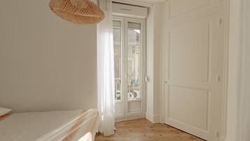 A bedroom with a bed, a hanging light fixture, a door, and a window.