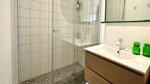 Une salle de bain avec une douche à parois de verre, un lavabo blanc avec un miroir et un distributeur de savon vert.