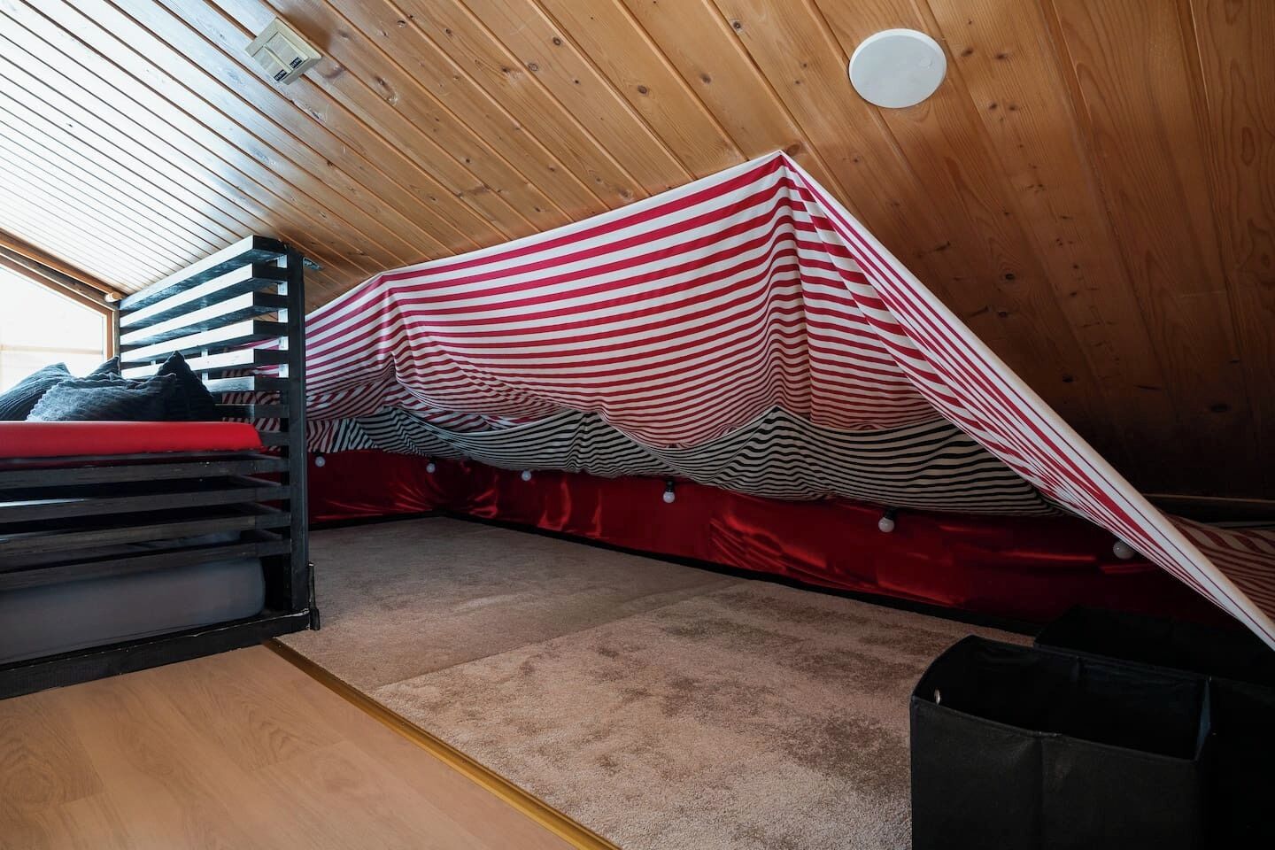 Un dormitorio acogedor en el ático con techo inclinado, una cama litera y un dosel a rayas.