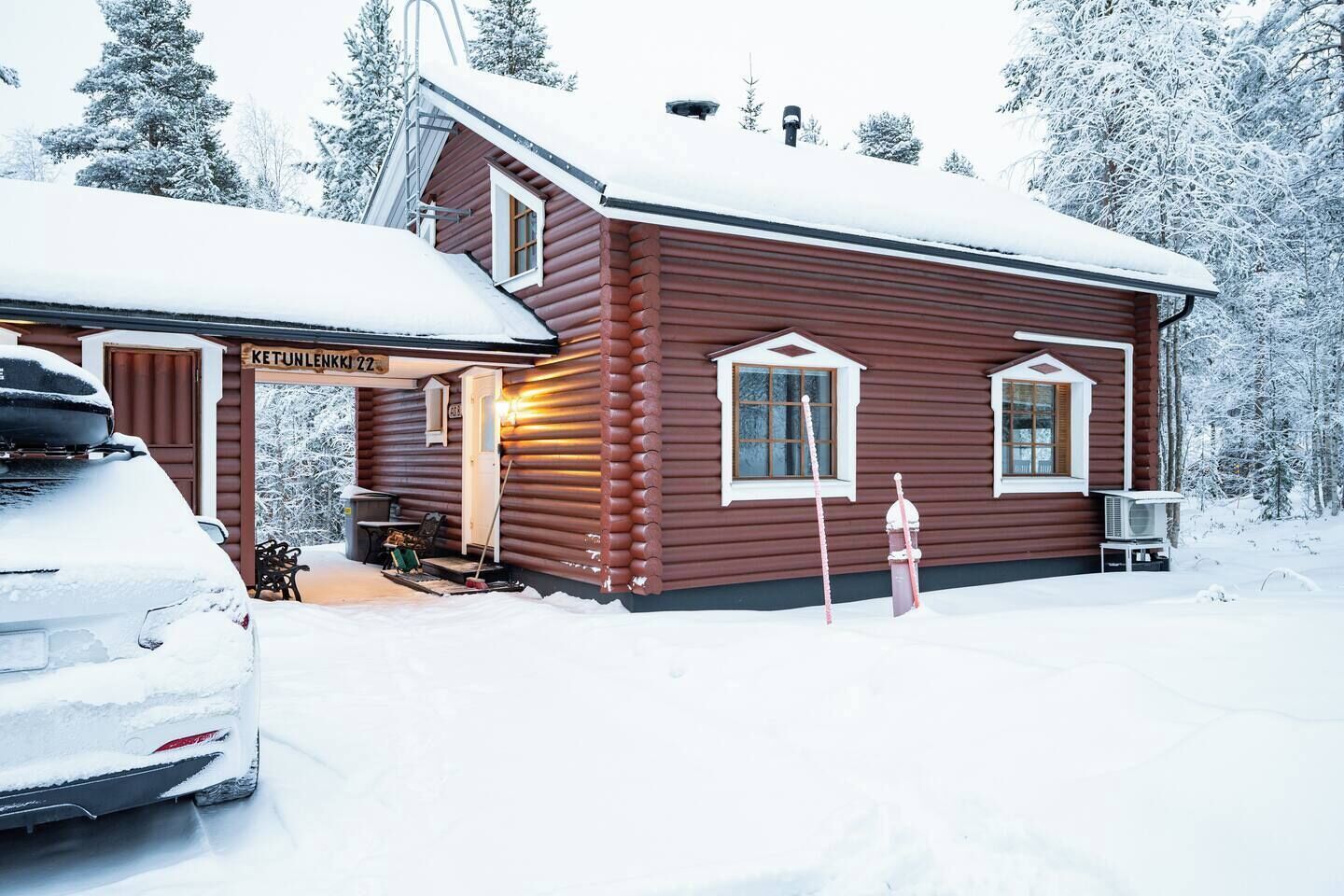 A log cabin with a covered porch, a car parked in front, and a snowy landscape.
