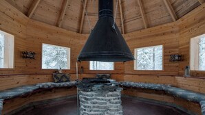 A log cabin interior with a stone fireplace, wooden walls, and large windows. - Alpine Fox by Aavalevi (Levi)
