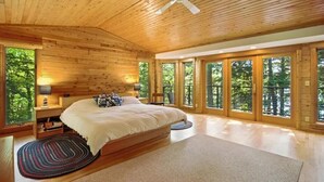 Un dormitorio amplio con una cama grande, paredes de madera y ventanas grandes que ofrecen vistas al bosque.
