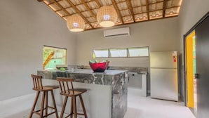 Une cuisine moderne avec un îlot en marbre, des tabourets de bar en bois, un saladier coloré et un réfrigérateur.