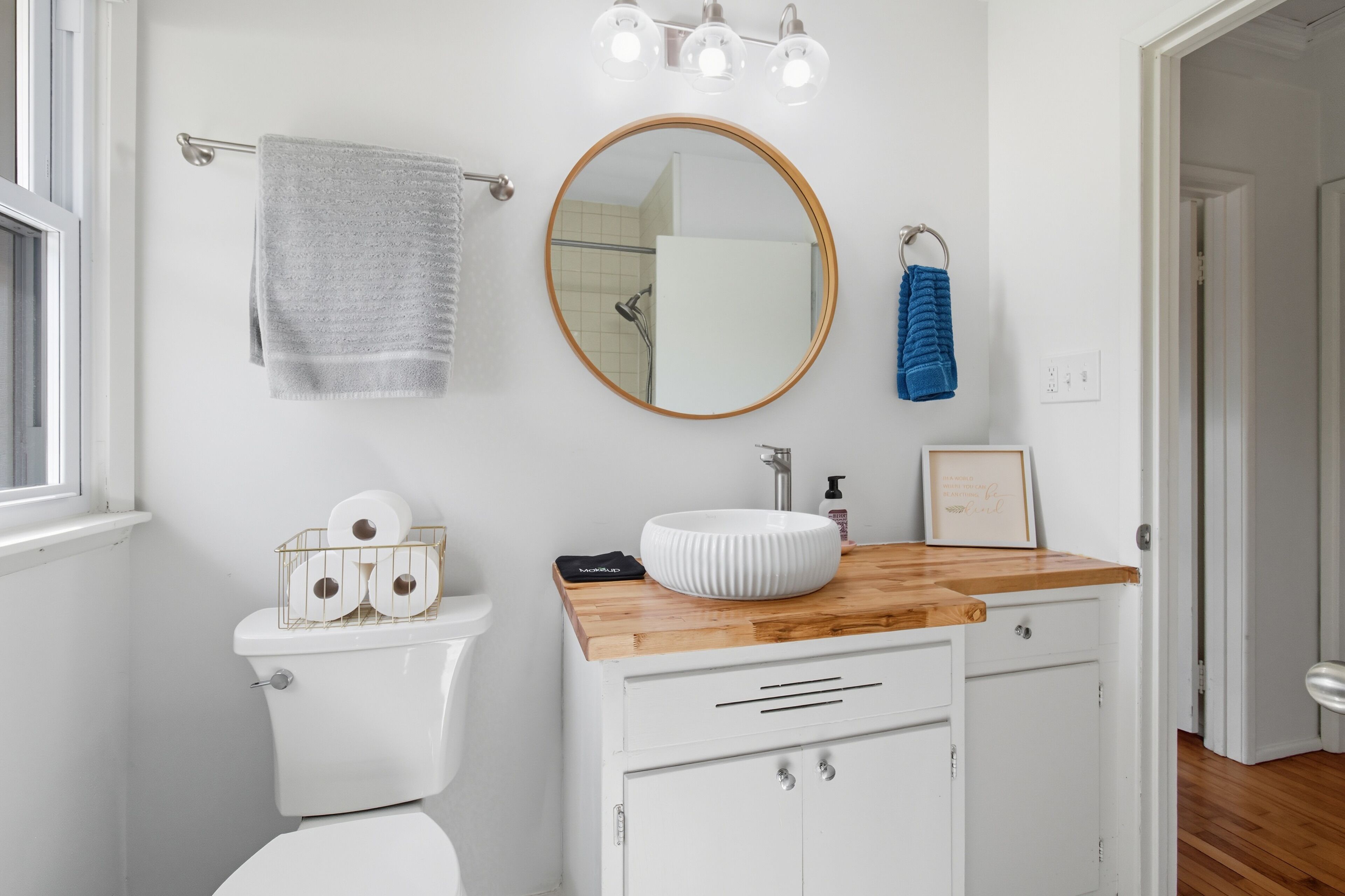 A bathroom with a toilet, a sink with a wooden countertop, a mirror, and a towel rack.