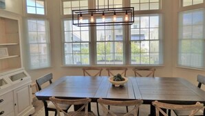 Un coin repas avec une grande table en bois, des chaises en osier, un saladier rempli de fruits et une suspension lumineuse.