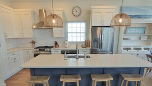 Une cuisine moderne avec des meubles blancs, un grand îlot central doté de tabourets, des appareils en acier inoxydable et un éclairage suspendu.