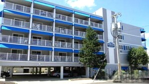 Un hotel de varios pisos con balcones, un estacionamiento y vista a la calle.