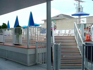 A covered outdoor area with steps leading to a pool area, a fence, and a utility pole. - Cozy Condo at Santa Barbara – Pool, Fitness Room & Balcony! (Ocean City)