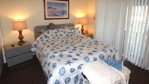 Habitación de hotel con una cama, dos mesitas de noche con lámparas, un cuadro enmarcado en la pared y una ventana con persianas.