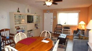 Una sala acogedora con una mesa de comedor de madera, sillas blancas, un sofá y un televisor.
