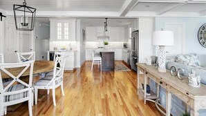 Un vaste espace de vie doté d’un plancher en bois, de meubles blancs, d’une table à manger et d’une cuisine située à l’arrière-plan.