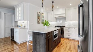 Une cuisine moderne avec des meubles blancs, un îlot central et un réfrigérateur en acier inoxydable.