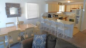 Un espace de vie compact comprenant un coin repas, une kitchenette et un canapé agrémenté d’un coussin à motifs.